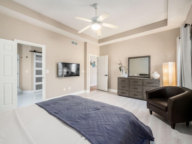 bedroom with visible vents, baseboards, a tray ceiling, light wood-style floors, and a ceiling fan