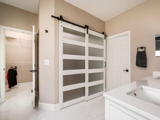 bathroom featuring a sink, a walk in closet, baseboards, and marble finish floor