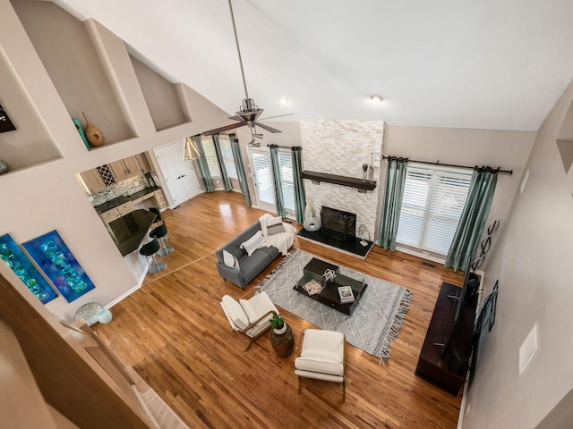 living room featuring high vaulted ceiling, a ceiling fan, wood finished floors, and a fireplace