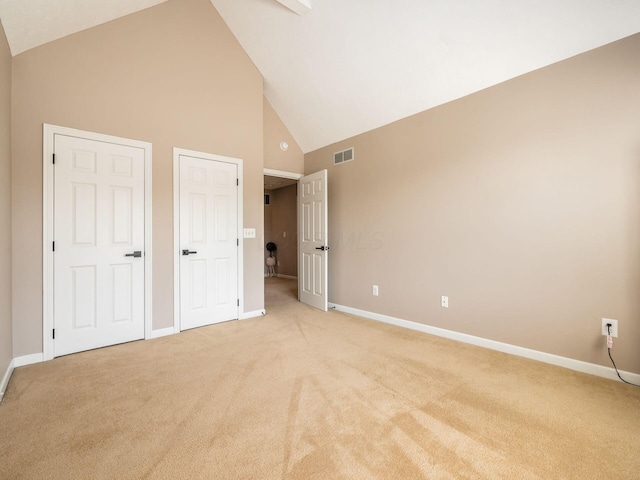 unfurnished bedroom with visible vents, baseboards, light colored carpet, and high vaulted ceiling