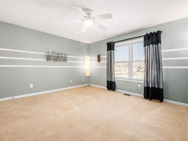 carpeted spare room with visible vents, baseboards, and a ceiling fan