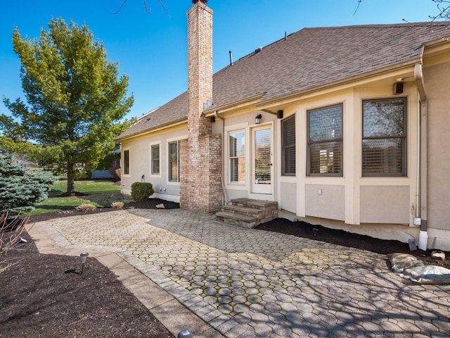 back of property with stucco siding, a patio, roof with shingles, and a chimney