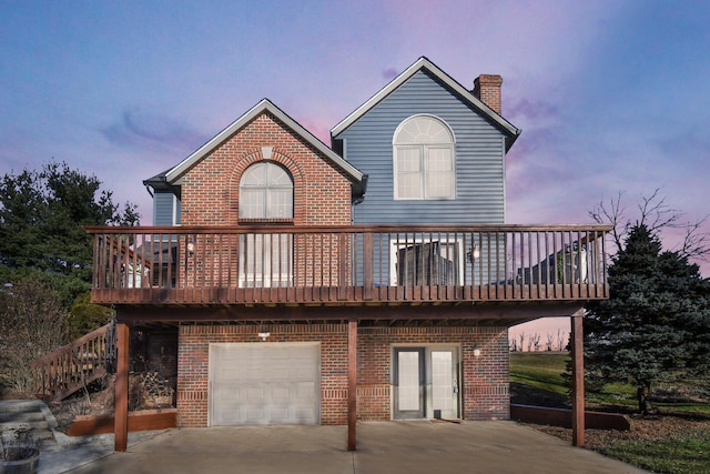 back of house at dusk with stairway, an attached garage, a chimney, concrete driveway, and brick siding