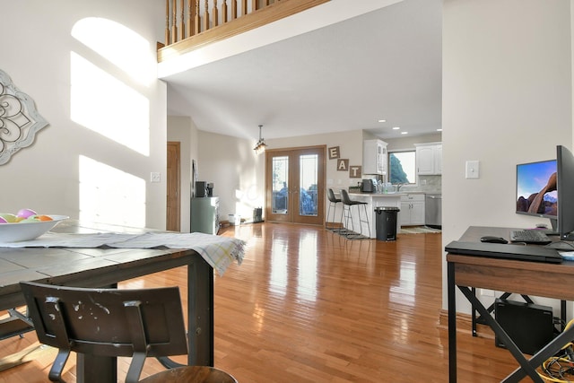 living room with french doors, light wood-style floors, and a towering ceiling