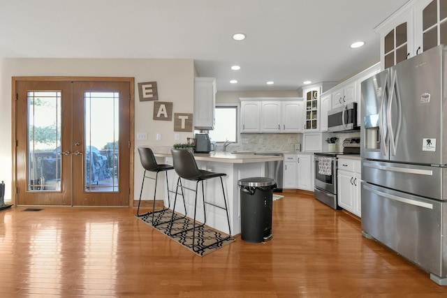 kitchen with a peninsula, plenty of natural light, glass insert cabinets, and stainless steel appliances