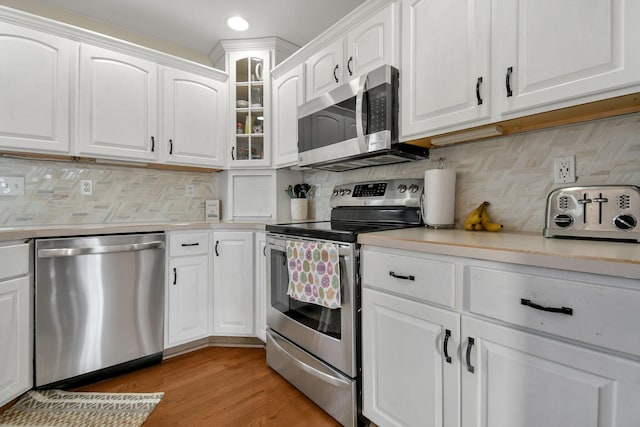 kitchen with tasteful backsplash, white cabinets, appliances with stainless steel finishes, and light countertops