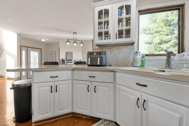 kitchen featuring tasteful backsplash, light countertops, a peninsula, white cabinets, and a sink