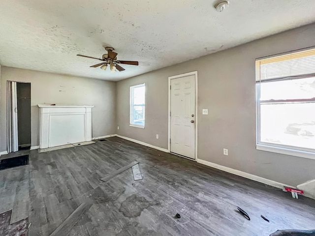 unfurnished living room with a textured ceiling, baseboards, a ceiling fan, and dark wood-style flooring