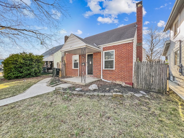 bungalow-style home with brick siding, a front yard, a chimney, and a patio area