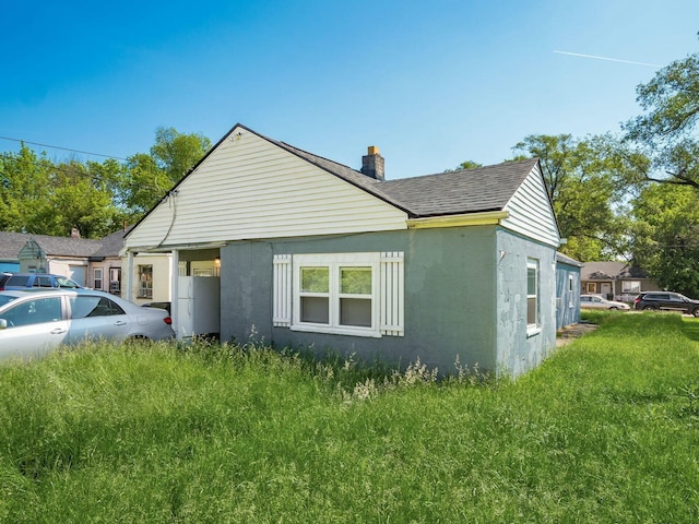 view of side of property featuring a chimney, stucco siding, and a shingled roof