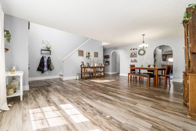 living room featuring stairs, baseboards, arched walkways, and light wood finished floors