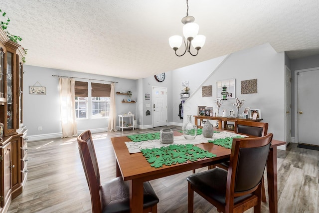 dining space with light wood-style floors, a chandelier, and a textured ceiling