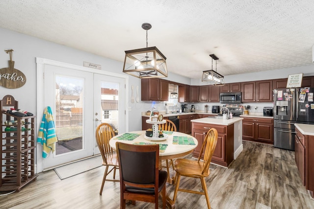 kitchen featuring stainless steel appliances, wood finished floors, a kitchen island with sink, and light countertops