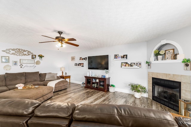 living room with a textured ceiling, wood finished floors, a ceiling fan, and a tile fireplace