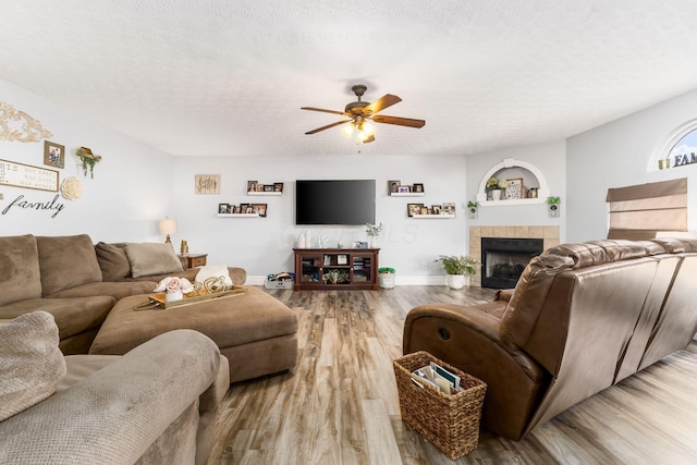 living area with wood finished floors, a ceiling fan, baseboards, a textured ceiling, and a tiled fireplace