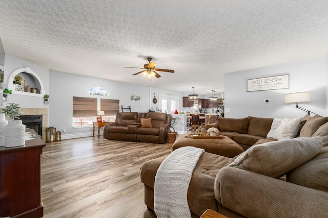 living room featuring wood finished floors, a textured ceiling, ceiling fan, and a tile fireplace