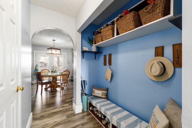 mudroom featuring baseboards, arched walkways, a textured ceiling, and wood finished floors