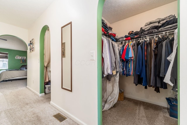 walk in closet featuring carpet flooring, arched walkways, and visible vents