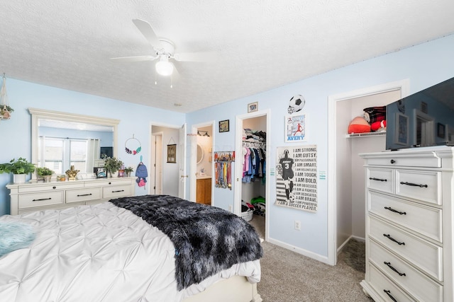 bedroom with baseboards, ceiling fan, a spacious closet, a textured ceiling, and light colored carpet