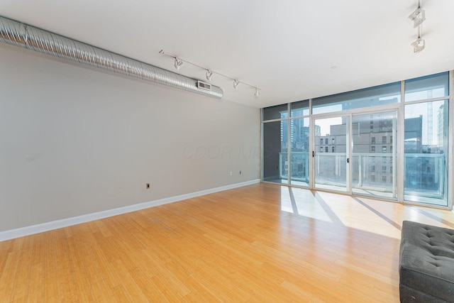 spare room with track lighting, floor to ceiling windows, light wood-type flooring, and baseboards