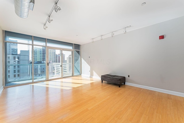 spare room with track lighting, a wall of windows, baseboards, and wood finished floors