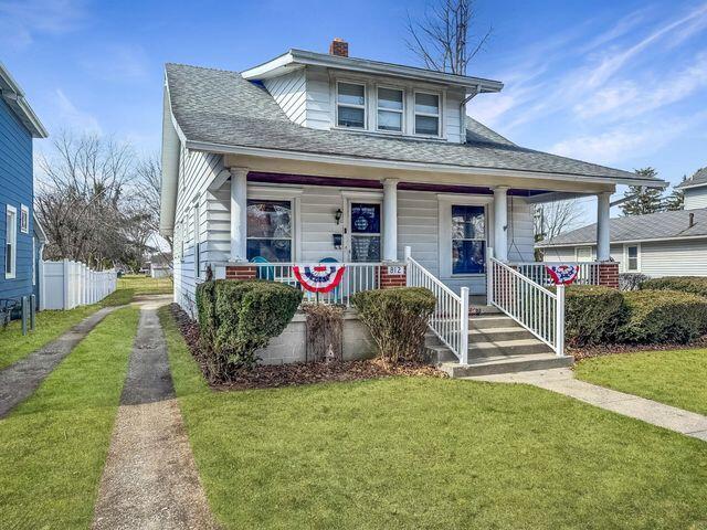 bungalow-style house featuring driveway, a front lawn, covered porch, a shingled roof, and a chimney