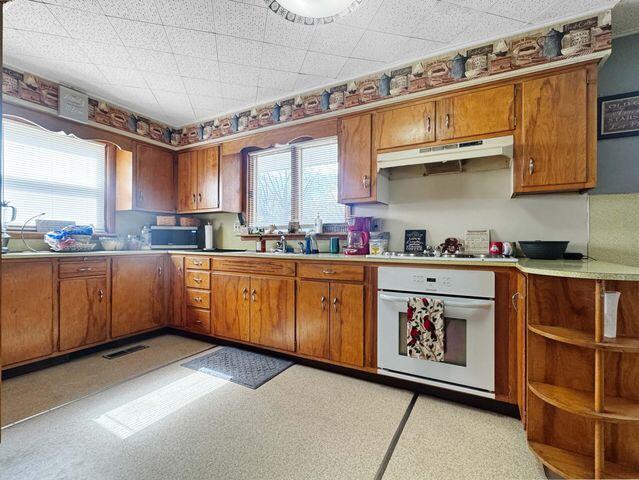 812 S Main St, Urbana, OH 43078 - kitchen featuring light countertops, brown cabinetry, under cabinet range hood, and oven