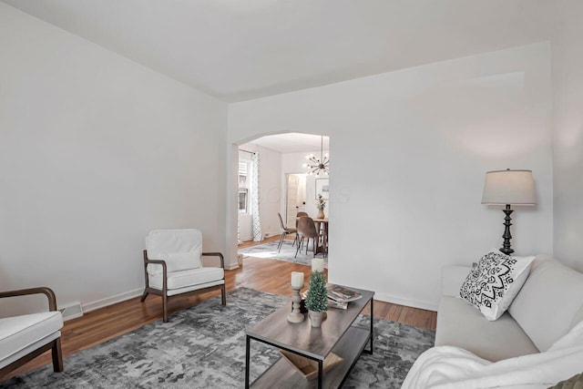 living area featuring arched walkways, a notable chandelier, baseboards, and wood finished floors