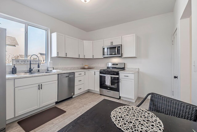 kitchen featuring a sink, stainless steel appliances, light countertops, and white cabinetry