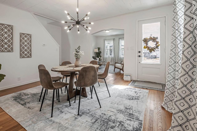 dining space featuring an inviting chandelier, wood finished floors, arched walkways, and ornamental molding