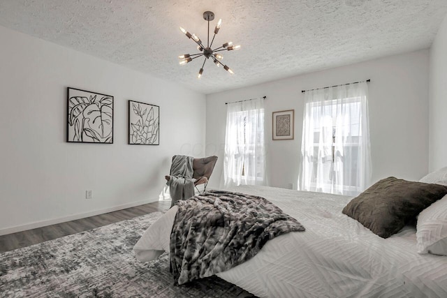 bedroom featuring a notable chandelier, a textured ceiling, baseboards, and wood finished floors