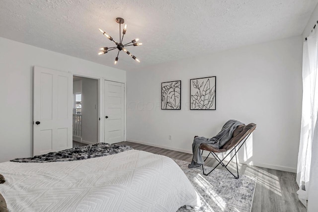 bedroom featuring a chandelier, a textured ceiling, baseboards, and wood finished floors