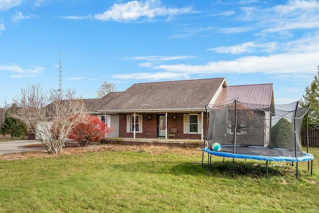 view of front of home with a front yard, a trampoline, brick siding, and a porch