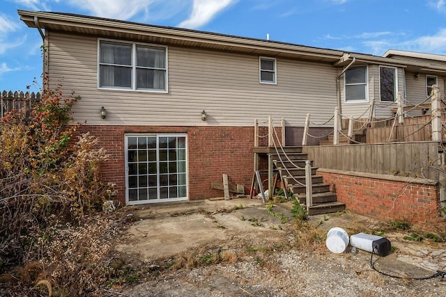 back of house featuring a patio, brick siding, stairs, and fence