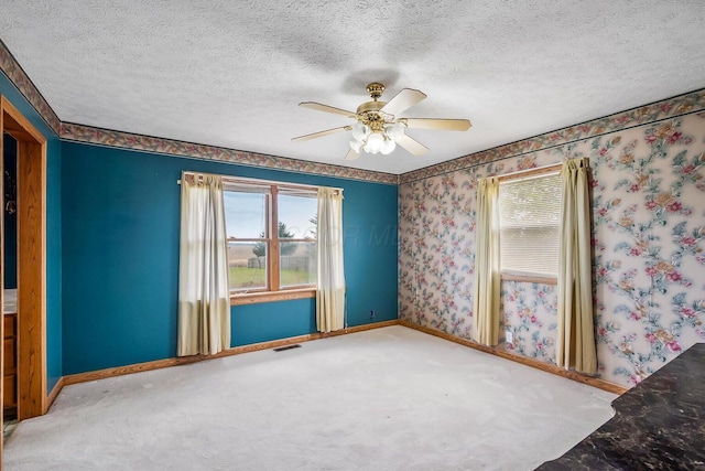carpeted empty room featuring a wealth of natural light, a textured ceiling, wallpapered walls, and baseboards