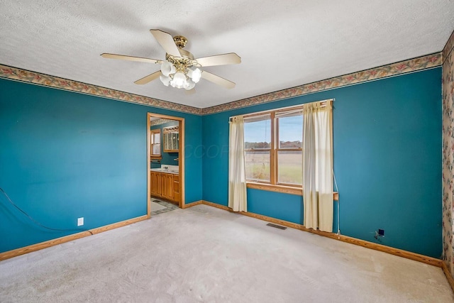 carpeted spare room with baseboards, a ceiling fan, visible vents, and a textured ceiling