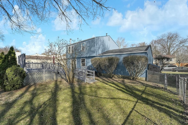 back of property with a wooden deck, a yard, and fence