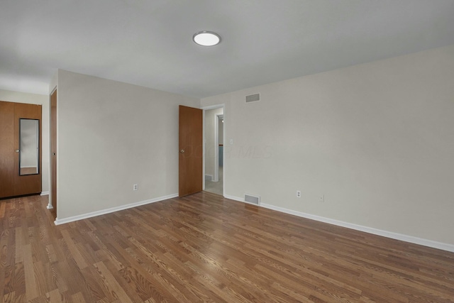 spare room featuring wood finished floors, visible vents, and baseboards