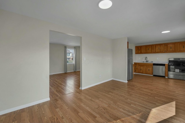 kitchen with light wood finished floors, appliances with stainless steel finishes, baseboards, and a sink