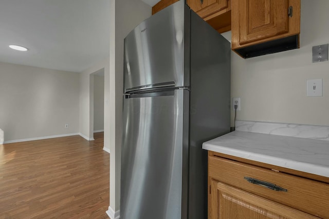 kitchen with wood finished floors, freestanding refrigerator, brown cabinetry, light countertops, and baseboards