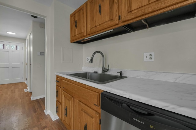 kitchen with a sink, dishwasher, light countertops, brown cabinets, and dark wood-style flooring