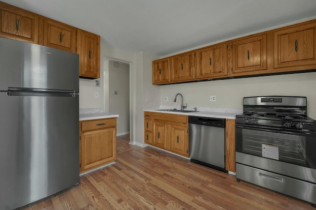 kitchen with light wood finished floors, light countertops, brown cabinetry, stainless steel appliances, and a sink