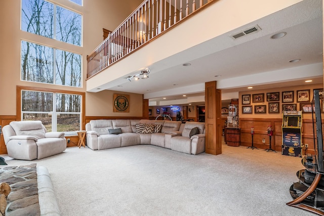 carpeted living area featuring visible vents, recessed lighting, a high ceiling, and a wainscoted wall