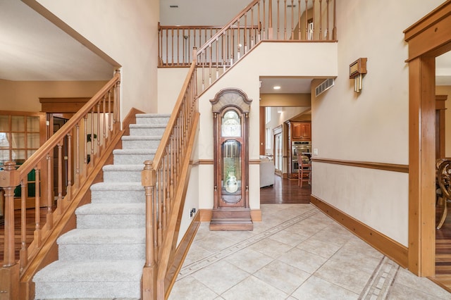 tiled foyer entrance featuring visible vents, baseboards, stairs, and a high ceiling