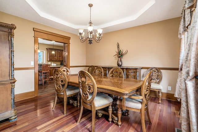 dining space with a tray ceiling, a notable chandelier, wood finished floors, and baseboards