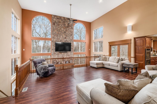 living room featuring wood finished floors, a ceiling fan, visible vents, and a towering ceiling