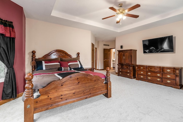 carpeted bedroom featuring a tray ceiling, a ceiling fan, and visible vents