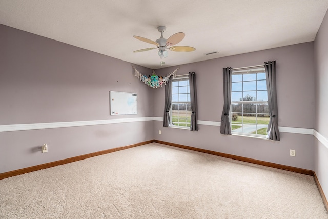 carpeted empty room with baseboards, visible vents, and ceiling fan