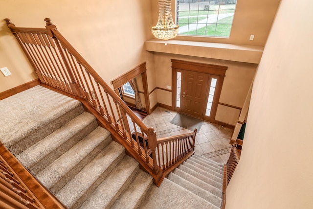 tiled entryway featuring baseboards, an inviting chandelier, a towering ceiling, and stairs