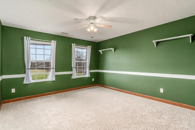 carpeted spare room with a textured ceiling, baseboards, visible vents, and ceiling fan